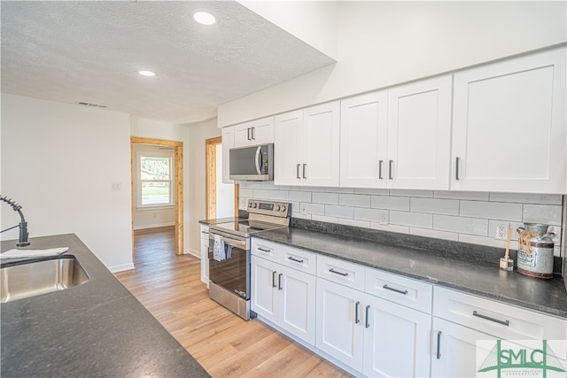 kitchen with white cabinets, backsplash, light hardwood / wood-style flooring, sink, and stainless steel appliances