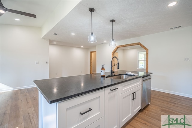 kitchen featuring dishwasher, an island with sink, light hardwood / wood-style floors, pendant lighting, and white cabinets