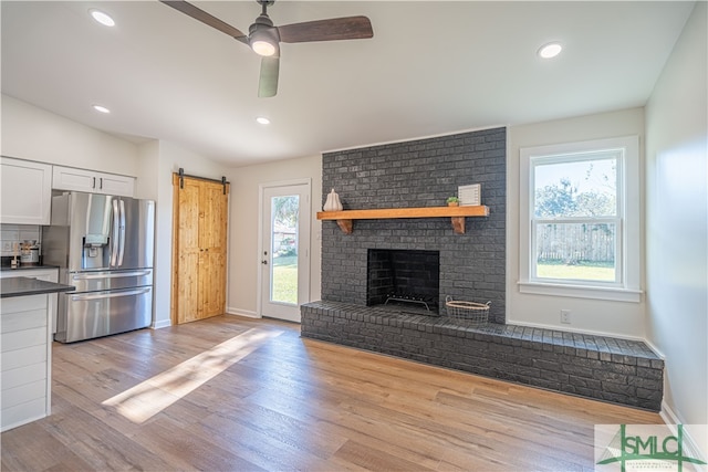 unfurnished living room featuring light wood-type flooring, vaulted ceiling, plenty of natural light, and a barn door