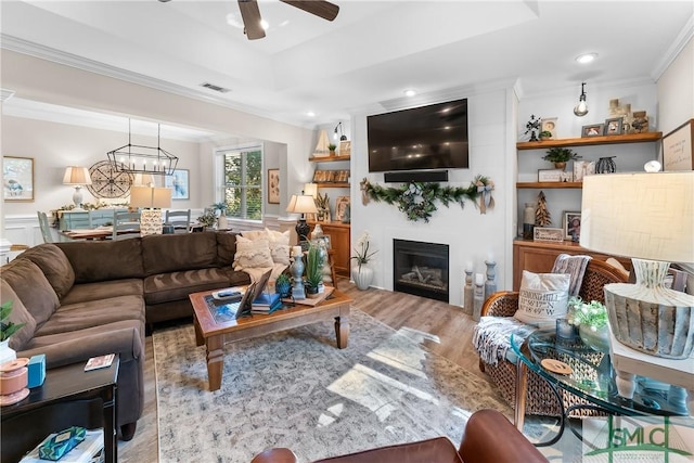 2203 River Oaks Dr, Richmond Hill, GA 31324 - living room featuring a glass covered fireplace, visible vents, ornamental molding, wood finished floors, and ceiling fan with notable chandelier