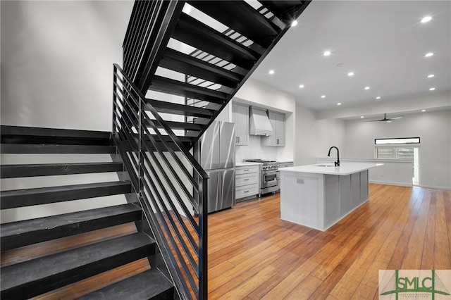 kitchen featuring appliances with stainless steel finishes, sink, light hardwood / wood-style floors, custom exhaust hood, and a kitchen island with sink