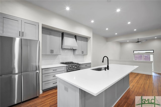 kitchen featuring dark wood-type flooring, an island with sink, sink, custom exhaust hood, and appliances with stainless steel finishes