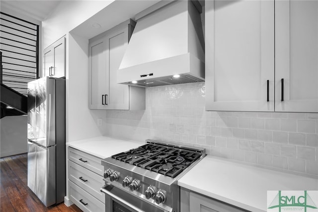 kitchen with dark wood-type flooring, tasteful backsplash, appliances with stainless steel finishes, and premium range hood