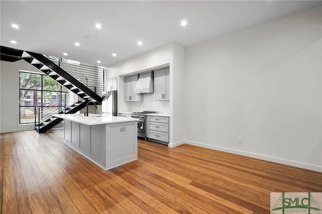 kitchen with appliances with stainless steel finishes, custom range hood, a kitchen island with sink, and light wood-type flooring