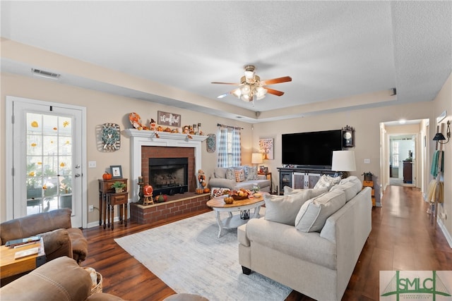 living room featuring ceiling fan, a textured ceiling, dark hardwood / wood-style flooring, and a brick fireplace