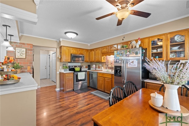 kitchen with hanging light fixtures, stainless steel appliances, sink, light wood-type flooring, and a textured ceiling