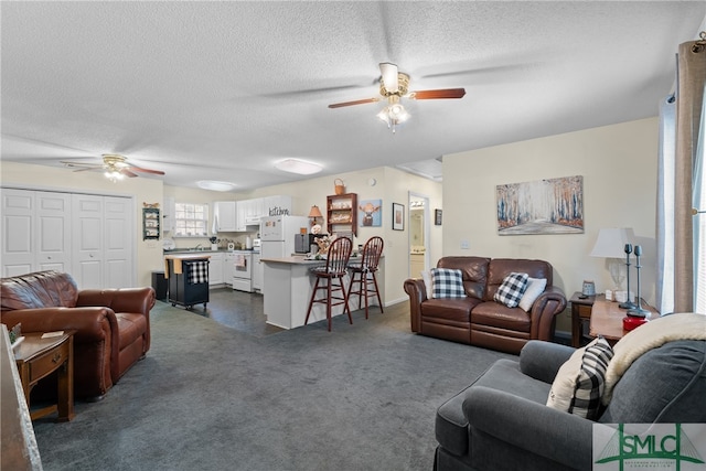 living room featuring ceiling fan, a textured ceiling, and dark carpet