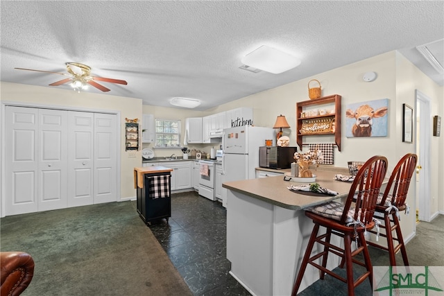 kitchen featuring white appliances, a kitchen bar, a textured ceiling, white cabinetry, and ceiling fan