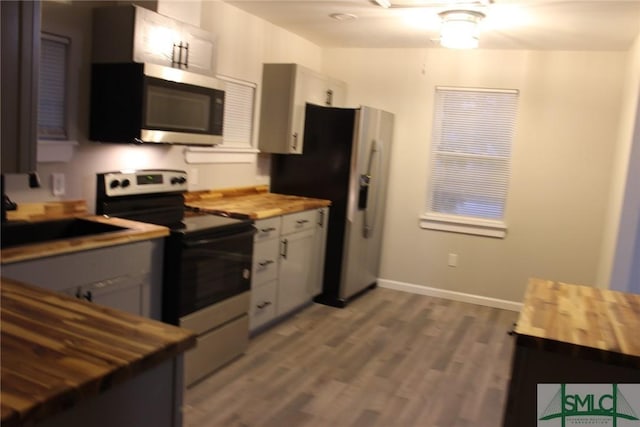 kitchen with stainless steel appliances, sink, wood-type flooring, white cabinets, and butcher block counters