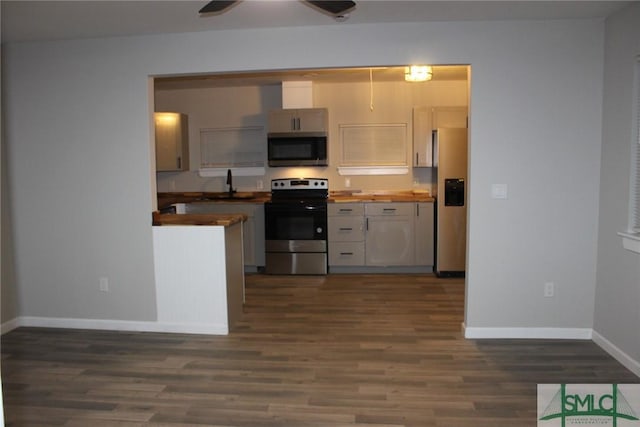 kitchen with a sink, butcher block counters, stainless steel appliances, baseboards, and dark wood-style flooring