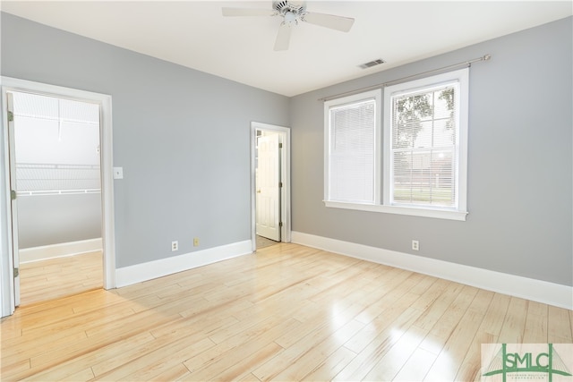 unfurnished bedroom with a walk in closet, a closet, light wood-type flooring, and ceiling fan