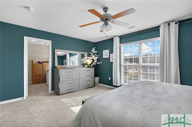 bedroom featuring ceiling fan, a textured ceiling, a closet, a walk in closet, and light colored carpet