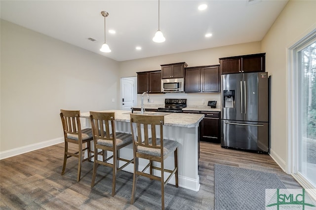 kitchen with dark hardwood / wood-style floors, a kitchen breakfast bar, an island with sink, pendant lighting, and appliances with stainless steel finishes