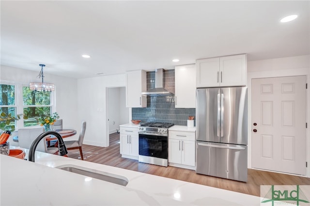 kitchen featuring wall chimney exhaust hood, stainless steel appliances, sink, decorative light fixtures, and white cabinetry