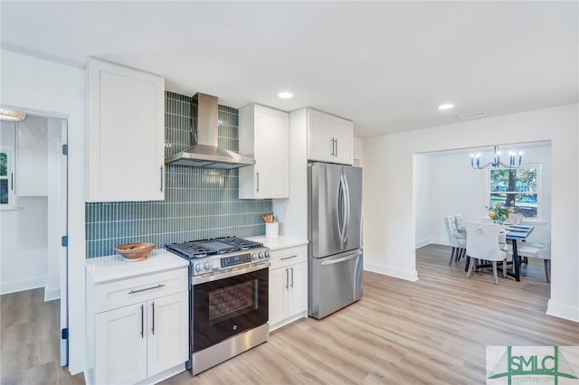 kitchen featuring appliances with stainless steel finishes, wall chimney range hood, light hardwood / wood-style floors, and white cabinets