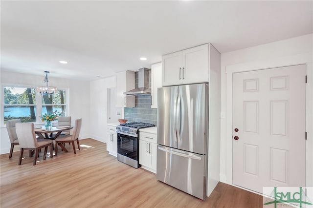 kitchen with appliances with stainless steel finishes, wall chimney exhaust hood, white cabinets, decorative backsplash, and light hardwood / wood-style flooring