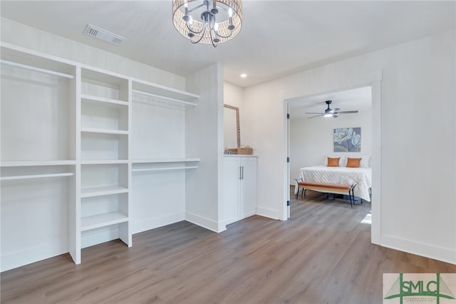 spacious closet with hardwood / wood-style flooring and ceiling fan with notable chandelier