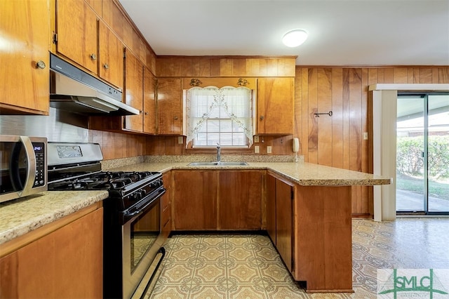 kitchen featuring gas stove, kitchen peninsula, wood walls, and sink