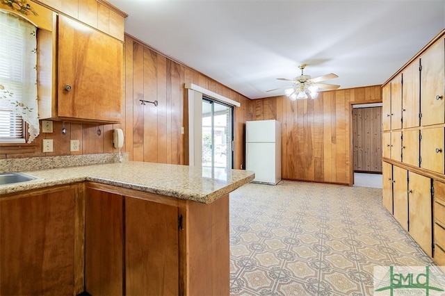 kitchen with kitchen peninsula, wood walls, ceiling fan, and white refrigerator