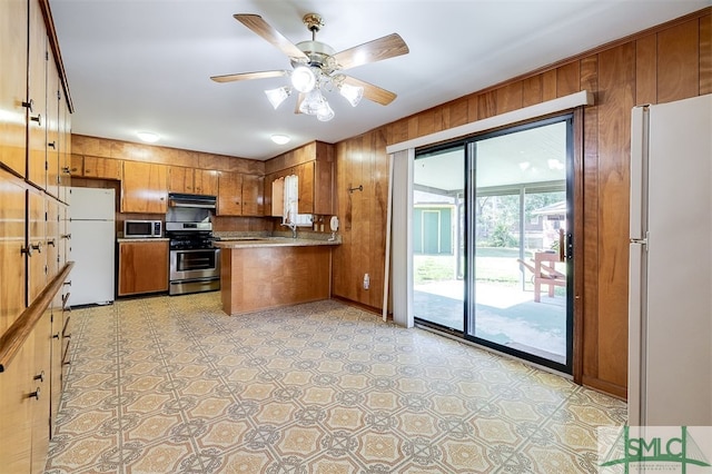 kitchen with appliances with stainless steel finishes, kitchen peninsula, wooden walls, and ceiling fan