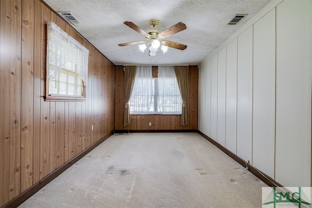 carpeted empty room featuring a textured ceiling, wooden walls, and ceiling fan