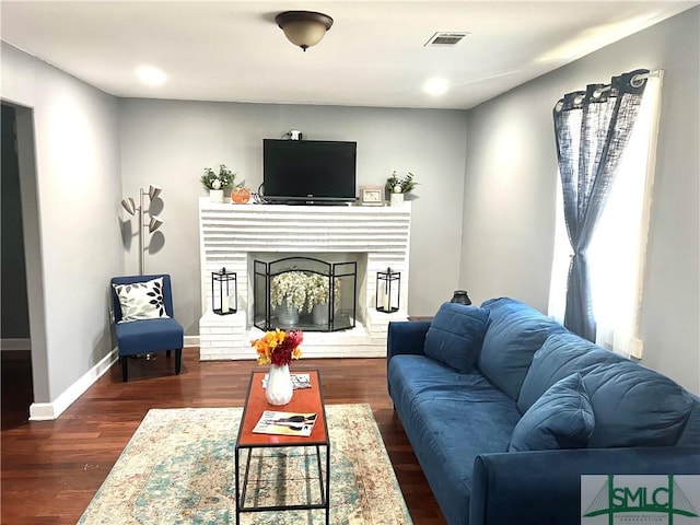 living area with visible vents, wood finished floors, baseboards, a fireplace with raised hearth, and recessed lighting