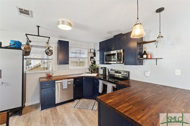 kitchen featuring appliances with stainless steel finishes, light wood-type flooring, wood counters, blue cabinets, and pendant lighting