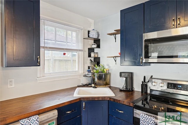 kitchen with appliances with stainless steel finishes, butcher block counters, sink, and blue cabinets