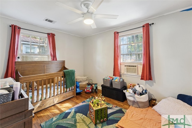 bedroom featuring ceiling fan, wood-type flooring, multiple windows, and a crib