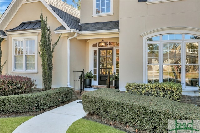 property entrance featuring metal roof, a shingled roof, a standing seam roof, and stucco siding