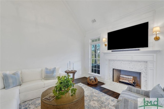 living room with a premium fireplace, wood finished floors, visible vents, baseboards, and vaulted ceiling