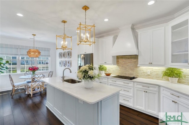 kitchen featuring a center island with sink, white cabinets, a sink, premium range hood, and black electric cooktop