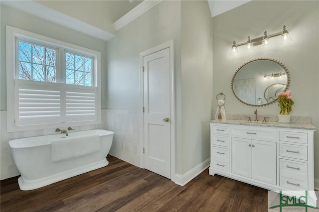 full bathroom with a freestanding bath, wood finished floors, vanity, and tile walls