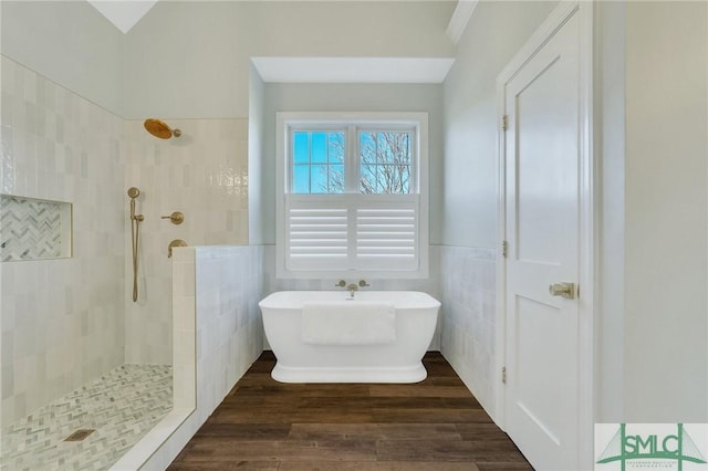 bathroom featuring a wainscoted wall, tile walls, a tile shower, wood finished floors, and a freestanding tub