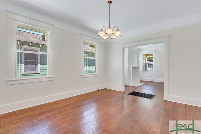 spare room featuring a notable chandelier, a healthy amount of sunlight, and dark hardwood / wood-style flooring