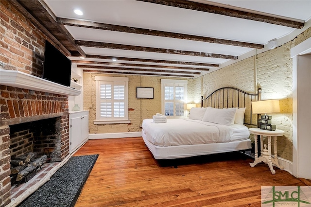 bedroom with a fireplace, beamed ceiling, brick wall, and hardwood / wood-style flooring