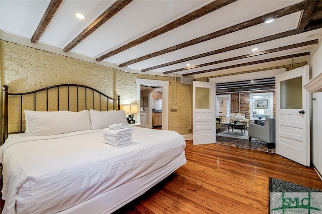 bedroom featuring beamed ceiling, hardwood / wood-style flooring, and brick wall