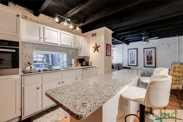 kitchen featuring track lighting, a kitchen breakfast bar, appliances with stainless steel finishes, light stone counters, and white cabinetry