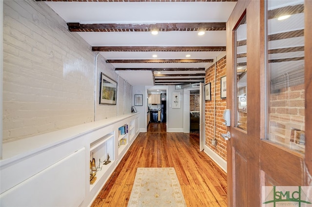 corridor with beamed ceiling, light hardwood / wood-style flooring, and brick wall