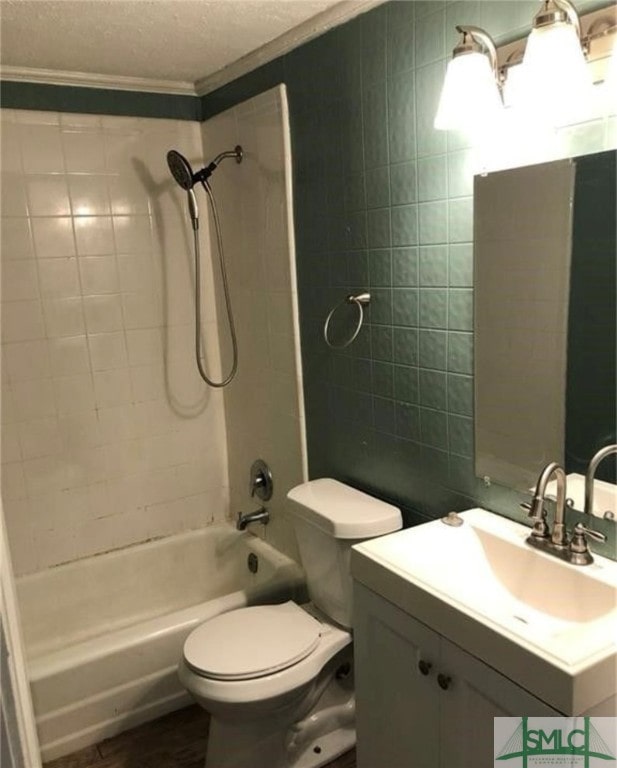 full bathroom featuring a textured ceiling, toilet, vanity, crown molding, and tiled shower / bath combo