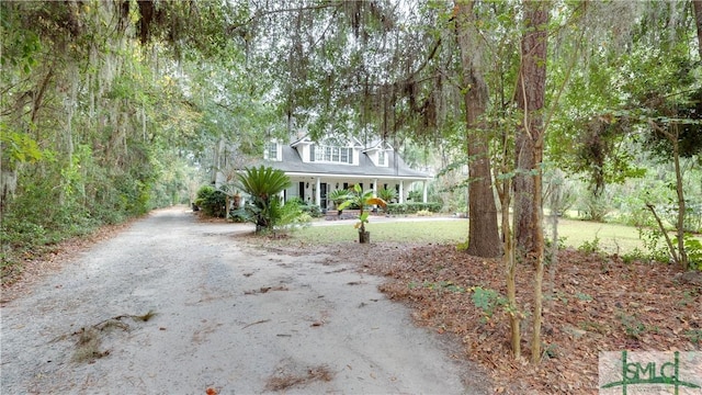 new england style home featuring covered porch, driveway, and a view of trees