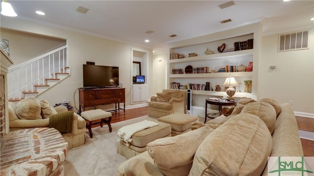 living room featuring visible vents, built in shelves, crown molding, and light wood finished floors