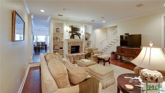 living room featuring hardwood / wood-style flooring, crown molding, a brick fireplace, and built in features