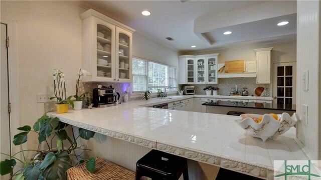 kitchen featuring glass insert cabinets, tasteful backsplash, a peninsula, and ornamental molding