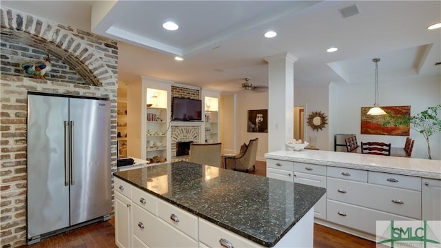 kitchen featuring dark wood-type flooring, a fireplace, high quality fridge, white cabinets, and a raised ceiling