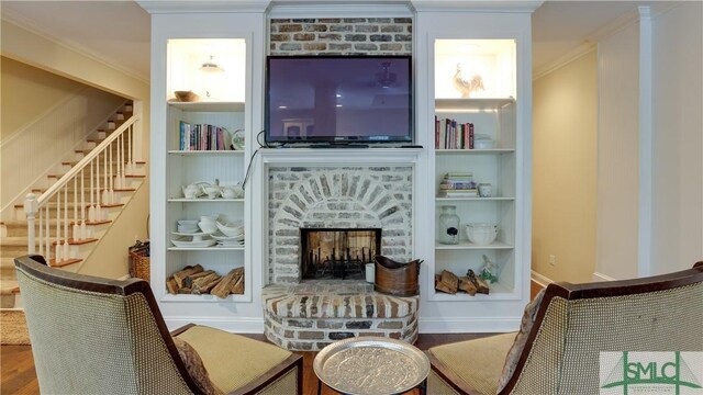 living room with a brick fireplace, built in features, ornamental molding, and hardwood / wood-style floors