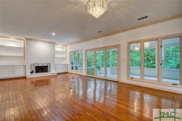 unfurnished living room with an inviting chandelier, a textured ceiling, hardwood / wood-style flooring, and a brick fireplace