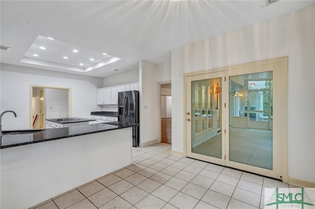 kitchen featuring white cabinets, a raised ceiling, dark stone counters, black fridge with ice dispenser, and sink