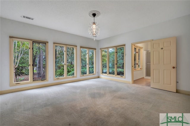 carpeted empty room featuring a notable chandelier, a textured ceiling, and a wealth of natural light