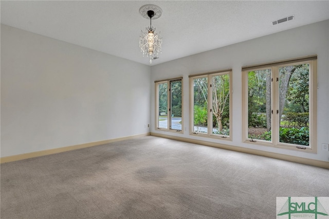 spare room with an inviting chandelier, a textured ceiling, and light colored carpet